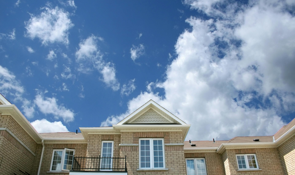 A modern brick house with large windows set against a bright blue sky with fluffy clouds.